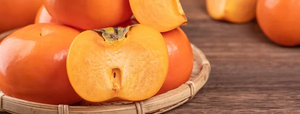 Frische, schöne orange Farbe persimmon Kaki auf Bambussieb über dunklem Holztisch. saisonale, traditionelle Früchte des chinesischen Mondneujahres aus nächster Nähe. — Stockfoto