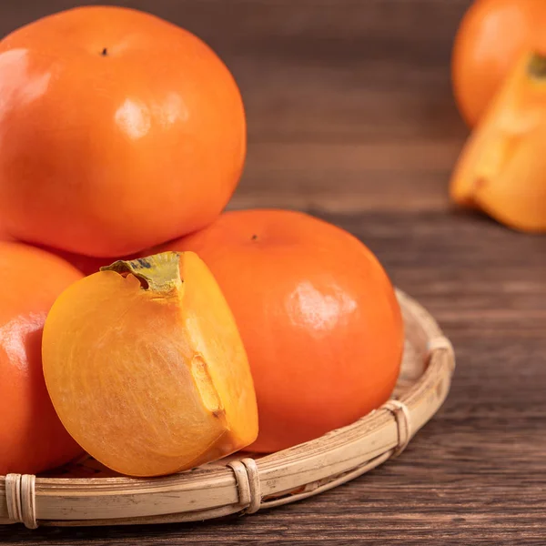 Frische, schöne orange Farbe persimmon Kaki auf Bambussieb über dunklem Holztisch. saisonale, traditionelle Früchte des chinesischen Mondneujahres aus nächster Nähe. — Stockfoto