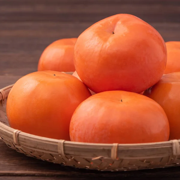 Frische, schöne orange Farbe persimmon Kaki auf Bambussieb über dunklem Holztisch. saisonale, traditionelle Früchte des chinesischen Mondneujahres aus nächster Nähe. — Stockfoto