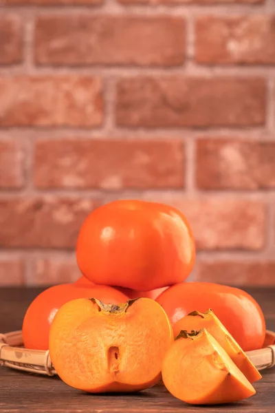 Fresh beautiful sliced sweet persimmon kaki on dark wooden table with red brick wall background, Chinese lunar new year fruit design concept, close up. — Stock Photo, Image