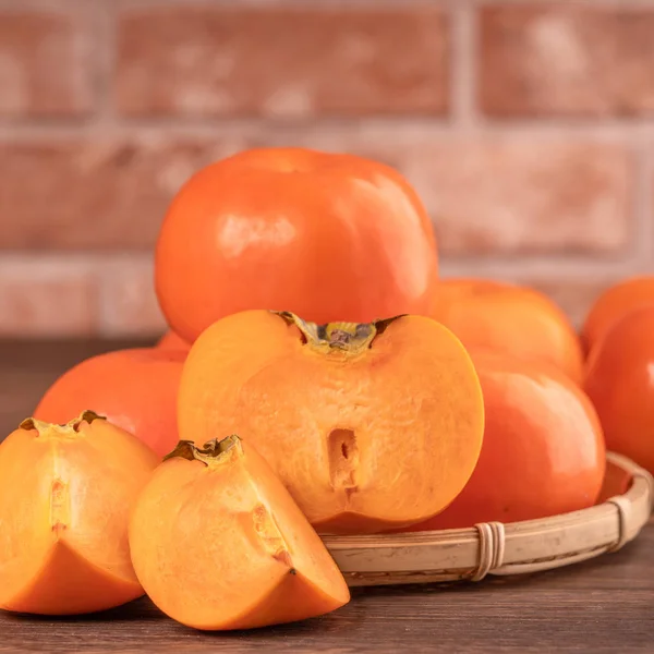 Frische schöne geschnittene süße Persimmon-Kaki auf dunklem Holztisch mit rotem Backsteinmauern-Hintergrund, chinesisches Mondneujahr-Fruchtdesign-Konzept, Nahaufnahme. — Stockfoto