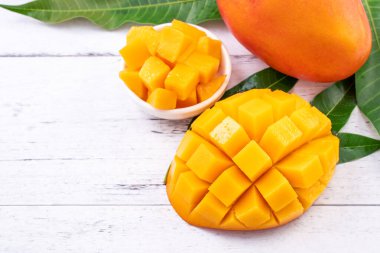 Taze mango, parlak ahşap masa arkasında yeşil yapraklı güzel doğranmış meyve. Tropik meyve tasarımı konsepti, kapat, kopyala.