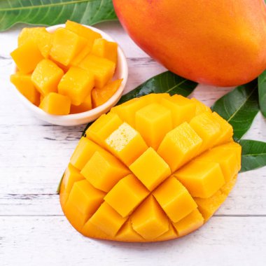 Taze mango, parlak ahşap masa arkasında yeşil yapraklı güzel doğranmış meyve. Tropik meyve tasarımı konsepti, kapat, kopyala.