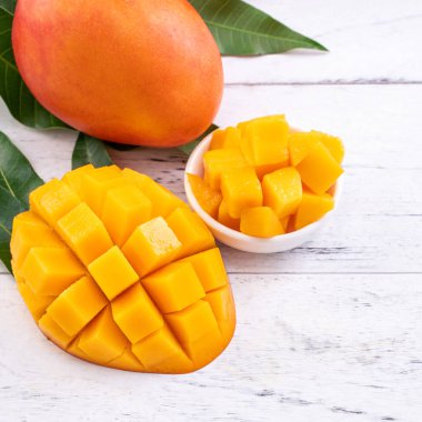 Taze mango, parlak ahşap masa arkasında yeşil yapraklı güzel doğranmış meyve. Tropik meyve tasarımı konsepti, kapat, kopyala.