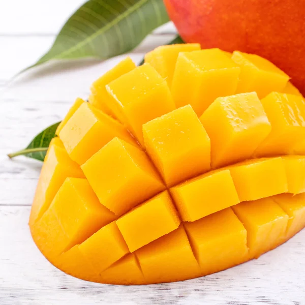 Frische Mango, schöne gehackte Früchte mit grünen Blättern auf hellem Holztischhintergrund. Design-Konzept für tropische Früchte, Nahaufnahme, Kopierraum. — Stockfoto