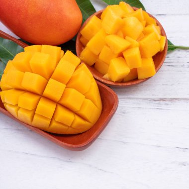 Taze mango, parlak ahşap masa arkasında yeşil yapraklı güzel doğranmış meyve. Tropik meyve tasarımı konsepti, kapat, kopyala.