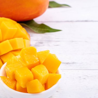 Taze mango, parlak ahşap masa arkasında yeşil yapraklı güzel doğranmış meyve. Tropik meyve tasarımı konsepti, kapat, kopyala.