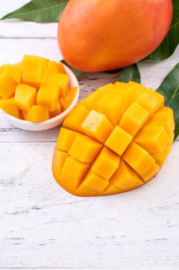 Taze mango, parlak ahşap masa arkasında yeşil yapraklı güzel doğranmış meyve. Tropik meyve tasarımı konsepti, kapat, kopyala.