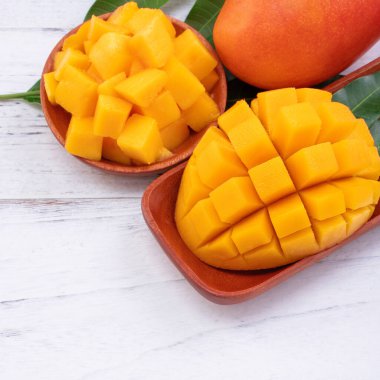 Taze mango, parlak ahşap masa arkasında yeşil yapraklı güzel doğranmış meyve. Tropik meyve tasarımı konsepti, kapat, kopyala.
