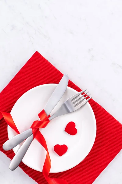 Valentine\'s Day, Mother\'s Day, holiday dating meal, banquet design concept - White plate and red ribbon on marble background, top view, flat lay.