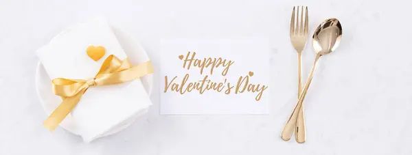 Valentine\'s Day holiday dating meal, banquet greeting card design concept - White plate and golden color tableware on marble background, top view, flat lay.