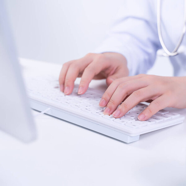 Business concept - Young female doctor woman working at office with computer, typing electronic medical record, white table background, close up, copy space