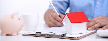 İş konsepti - Mavi gömlekli genç Asyalı adam ev kredisi ödemesi, ödeme sigortası, vergi ödeme anlaşmasını hesaplar, imzalar, kapatır.