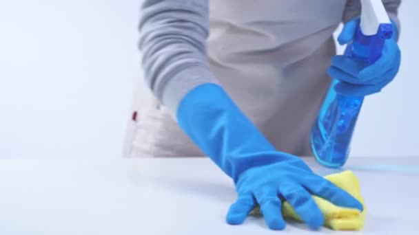 Junge Haushälterin in Schürze putzt, wischt mit blauen Handschuhen die Tischfläche ab, feuchter gelber Lappen, Sprühflaschenreiniger, Nahaufnahme, 4K-Nahaufnahme, leeres Designkonzept.
