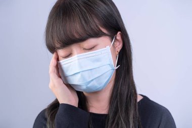 Genç kadın sersemlemiş, baş ağrısı, hasta, hasta, gri arka planda tıbbi mavi bir maske takıyor, yakın plan, kopyalama alanı.