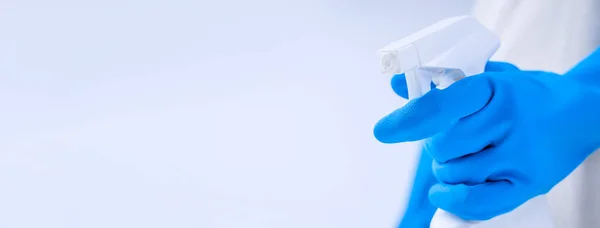 Young woman housekeeper in apron is doing cleaning with blue gloves, wet yellow rag, spraying bottle cleaner, close up, copy space, blank design concept.