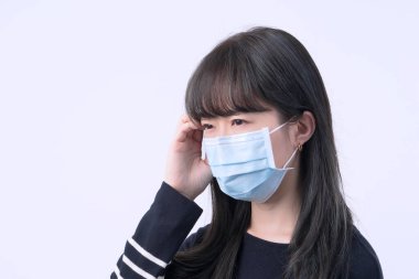 Genç kadın sersemlemiş, baş ağrısı, hasta, hasta, gri arka planda tıbbi mavi bir maske takıyor, yakın plan, kopyalama alanı.