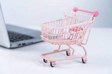 İnternetten alışveriş. Mini boş pembe market arabası beyaz masa arkaplanındaki dizüstü bilgisayarın üzerinde, ev konsepti satın alarak, kapat.