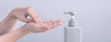 El yıkama. Asyalı genç bir kadın ellerini yıkamak için sıvı sabun kullanıyor, koruyucu pandemik koronavirüs konsepti gri beyaz arka planda izole edilmiş, kapatın..