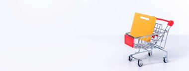 Beyaz masa arkasında izole edilmiş gümüş bir alışveriş arabasında alışveriş torbaları, evde kalma konsepti, yakın plan, uzay tasarımını kopyala.