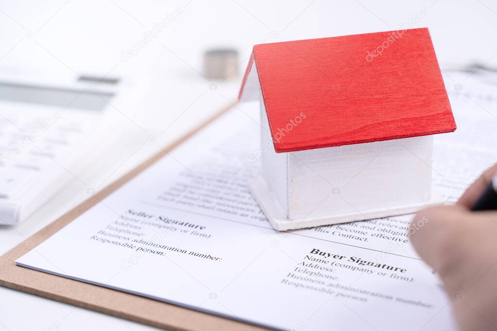 Business concept - Young Asian man in blue shirt calculates, signs agreement contract to buy a house loan payment, paying insurance, tax, close up.