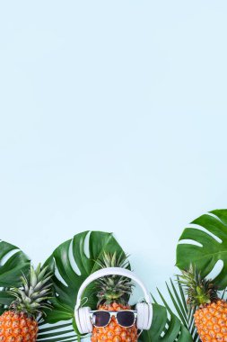 Beyaz kulaklık takan komik ananas, müzik dinleme konsepti, tropik palmiye yaprakları ile mavi arka planda izole edilmiş, üst görünüm, düz dizayn.