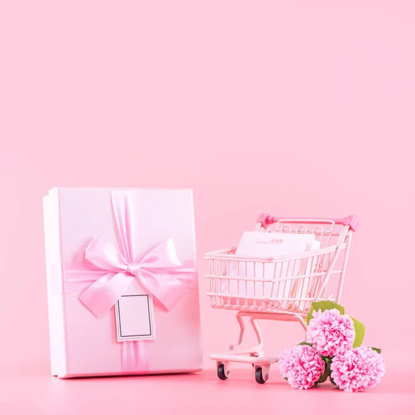 Mother's Day holiday gift design concept, pink carnation flower bouquet with wrapped box isolated on light pink background, copy space.