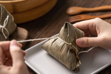 Pirinç hamuru zongzi yiyor - Genç Asyalı kadın geleneksel Çin yemeklerini evde ahşap masada yiyor Ejderha Teknesi Festivali için, kapatın