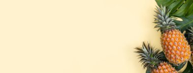 Tropikal palmiye yaprakları üzerinde güzel ananas parlak pastel sarı arka planda izole edilmiş, üst manzara, düz yer, yaz meyvelerinin üzerinde.