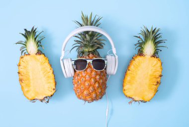 Beyaz kulaklık takan komik ananas, müzik dinleme konsepti, tropik palmiye yaprakları ile izole edilmiş renkli arka plan, üst görünüm, düz dizayn.
