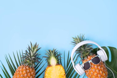 Beyaz kulaklık takan komik ananas, müzik dinleme konsepti, tropik palmiye yaprakları ile izole edilmiş renkli arka plan, üst görünüm, düz dizayn.