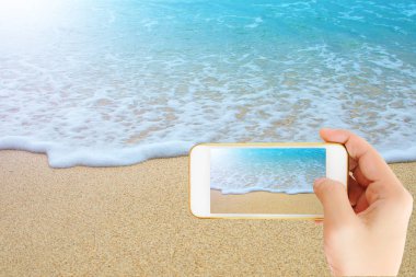 Elini tut güzel mavi deniz ve kum, seyahat konsepti ile akıllı telefon. tuch ekran kırpma yolu ile.