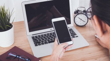 Kadın el smartphone ve dizüstü bilgisayar arka plan kullanarak işyeri tablodur