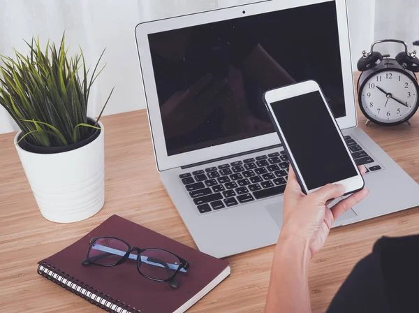 Kadın el smartphone ve dizüstü bilgisayar arka plan kullanarak işyeri tablodur