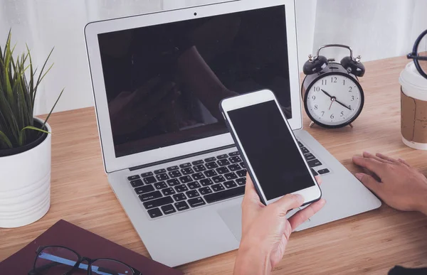 Kadın el smartphone ve dizüstü bilgisayar arka plan kullanarak işyeri tablodur