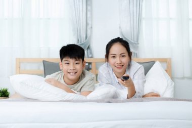 Asyalı kadın yatakta televizyon izlerken Asya çocukla.