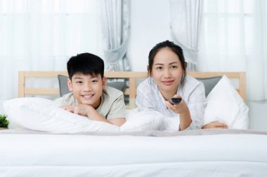 Asyalı kadın yatakta televizyon izlerken Asya çocukla.