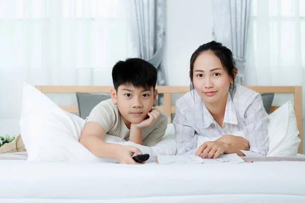 Asyalı kadın yatakta televizyon izlerken Asya çocukla.