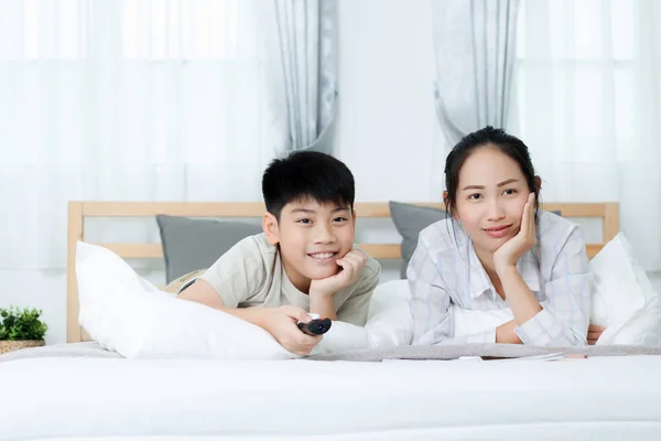 Aziatische vrouw met Aziatische jongen televisiekijken op bed. — Stockfoto