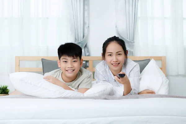 Aziatische vrouw met Aziatische jongen televisiekijken op bed. — Stockfoto