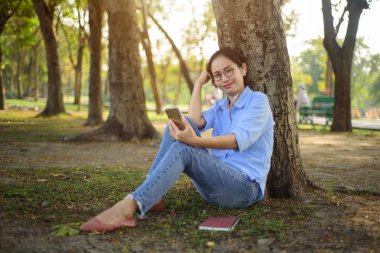 Asyalı kadın ağaç altında smartphone üzerinden müzik dinleme