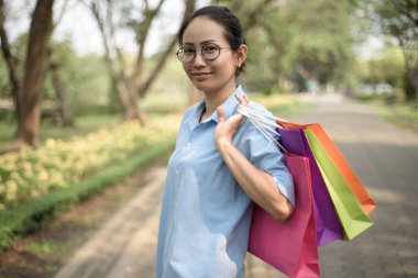 Asyalı kadın parkta yürürken alışveriş torbaları holding.