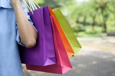 Asyalı kadın parkta yürürken alışveriş torbaları holding.
