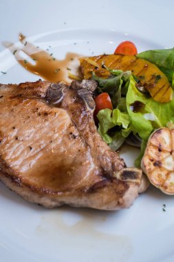Izgara domuz biftek. Beyaz tabakta taze kişniş ile serpilir şeritler ile lezzetli ızgara domuz pirzola,