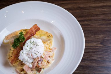 Ahşap arka plan üzerinde beyaz bir tabakta pastırma ve yumurta sarısı ile makarna. Spagetti ile tavada kızartılmış tepesinde kızarmış yumurta.