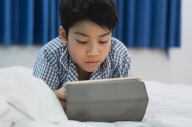 Kesici çocuk masada yatıyordu. Yatağın üzerinde dijital tabletle oynayan çocuk.