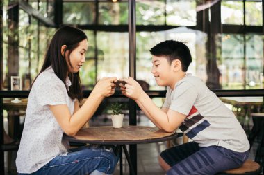 Asyalı çocukla birlikte Asyalı bir kadın kafede akıllı telefondan oyun oynuyor.