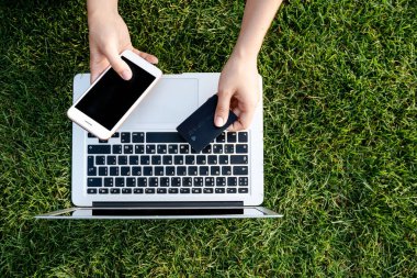 Kredi kartı, kredi kartı, internet üzerinden alışveriş, modern dijital teknoloji, nakit para, dizüstü bilgisayar, akıllı cep telefonu ve yeşil çim arka planda siyah kart. 