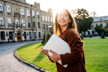 Charming young woman student in move walking in university garden with laptop computer, going to her classroom, beautiful sunset background, positive emotions, lifestyle people  clipart