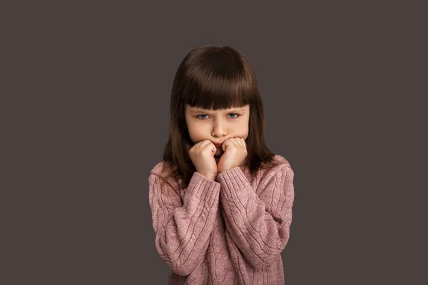 Depresyonda olan küçük kız çocuğu, kollarını kavuşturup, gri arka planda somurtan yanaklarıyla yüzünü kavuşturdu.